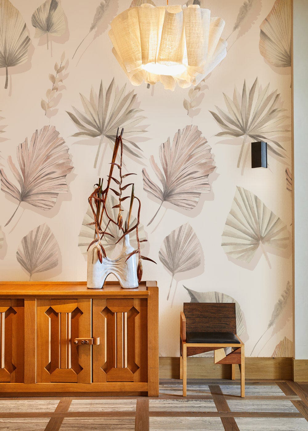 Elegant pastel botanical leaf wallpaper in contemporary interior with wooden cabinet, modern chair, floor lamp.