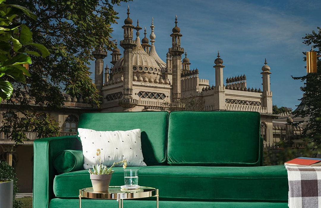Vintage mural wallpaper featuring historic palace, green velvet sofa, ornate side table, lush landscape view.