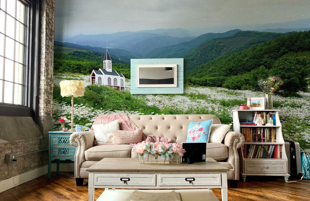 Charming mural wallpaper featuring church, alongside beige sofa, rustic coffee table, and wooden flooring in living room.