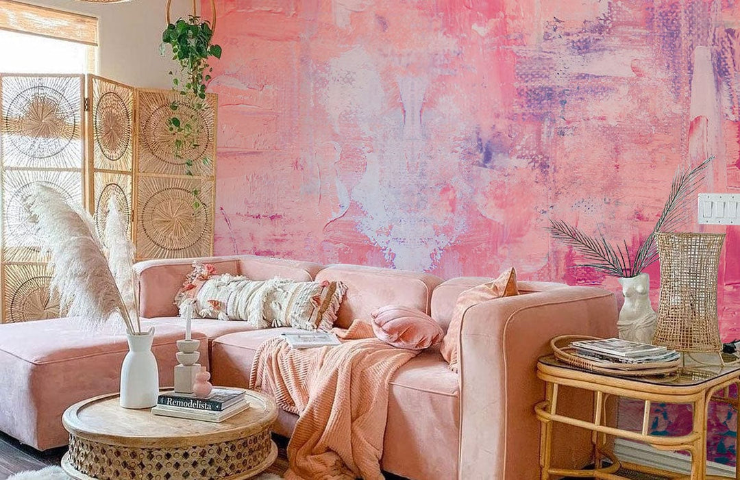Abstract pastel mural wallpaper complements pink sofa, wicker furniture, wooden accents, and natural decor items.