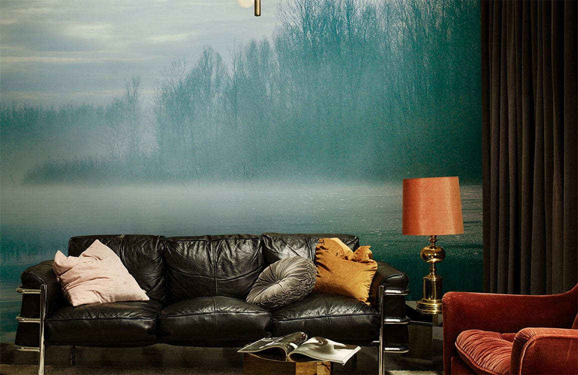 Misty teal forest mural wallpaper, black leather sofa, rust armchair, orange lamp in a cosy living room.