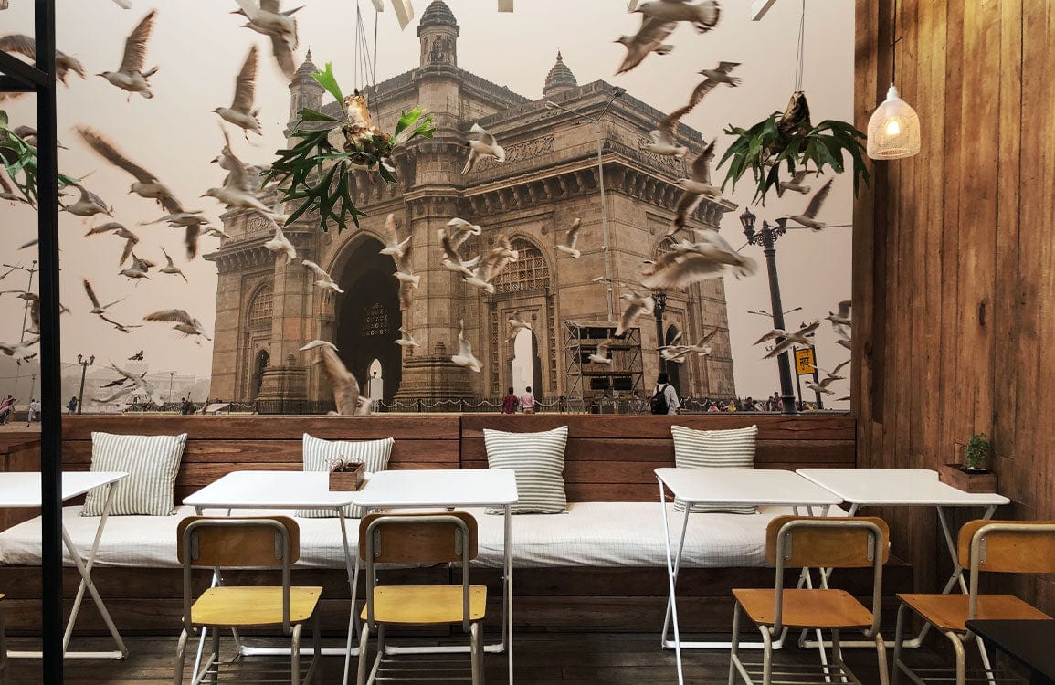 Vintage Gateway of India mural wallpaper, soaring birds; cafe with wooden chairs, white tables, hanging lights.