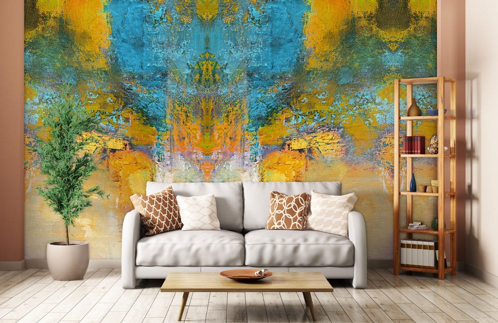 Abstract blue and gold mural wallpaper in modern living room with grey sofa, wooden floor, plant.
