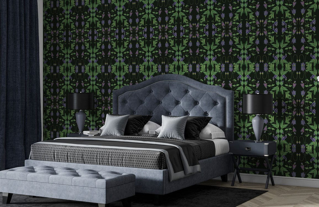 Dark botanical wallpaper; vibrant green foliage; grey upholstered bed and ottoman; bedroom with dark lamps.