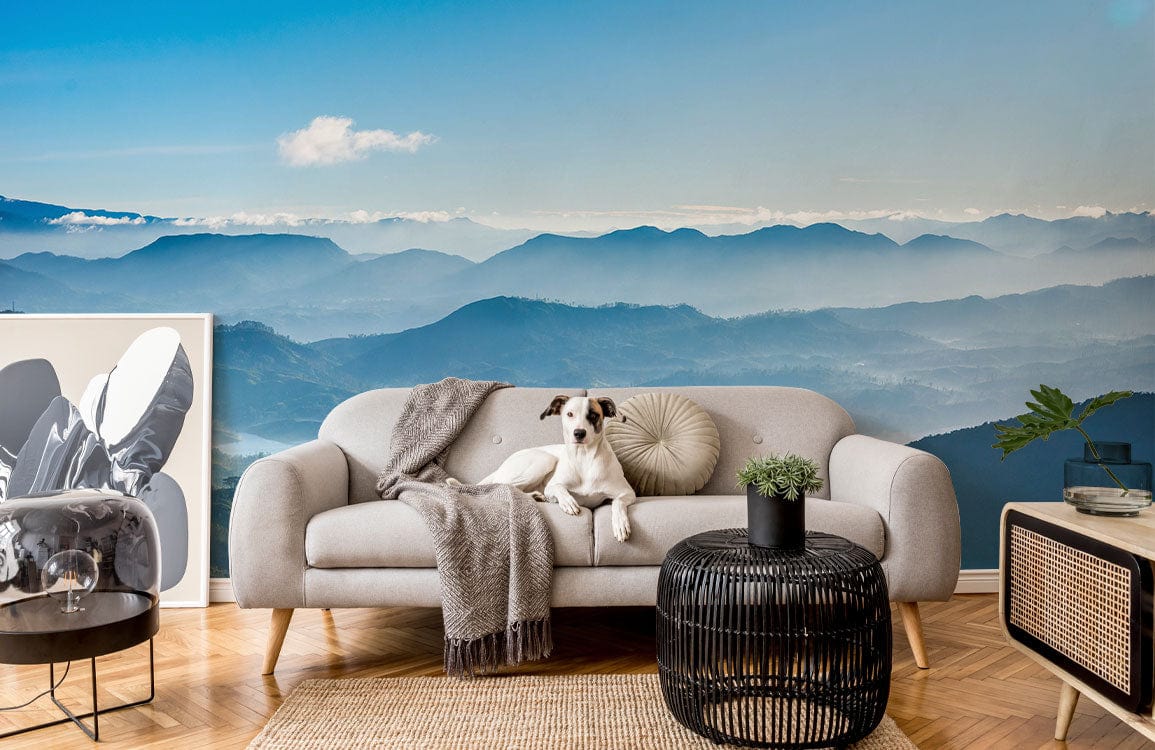 Grey sofa, Serene Blue Misty Mountain Mural Wallpaper, wicker ottoman, wooden flooring, tranquil living space.