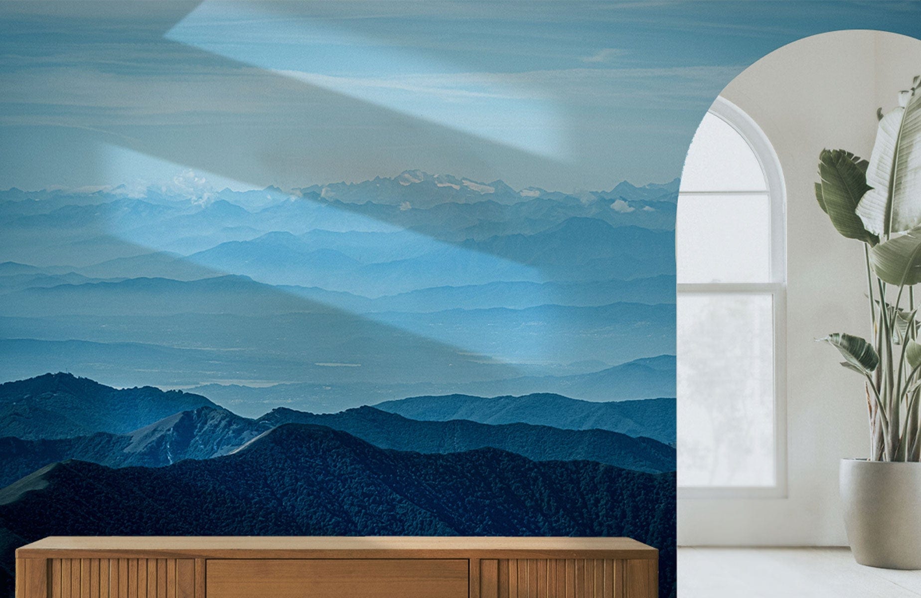Tranquil blue mountain landscape wallpaper in serene room with wooden cabinet and large plant.