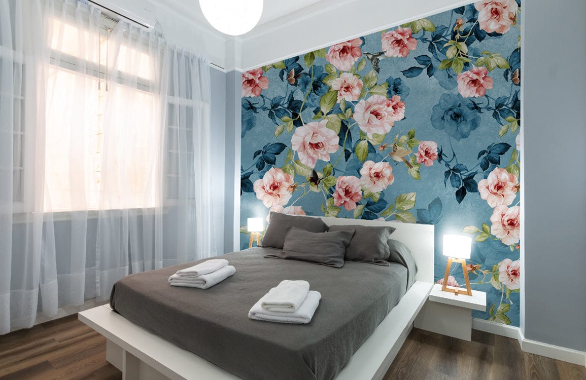Elegant bedroom with blue-pink floral wallpaper, grey bed, sheer curtains, and wooden flooring.