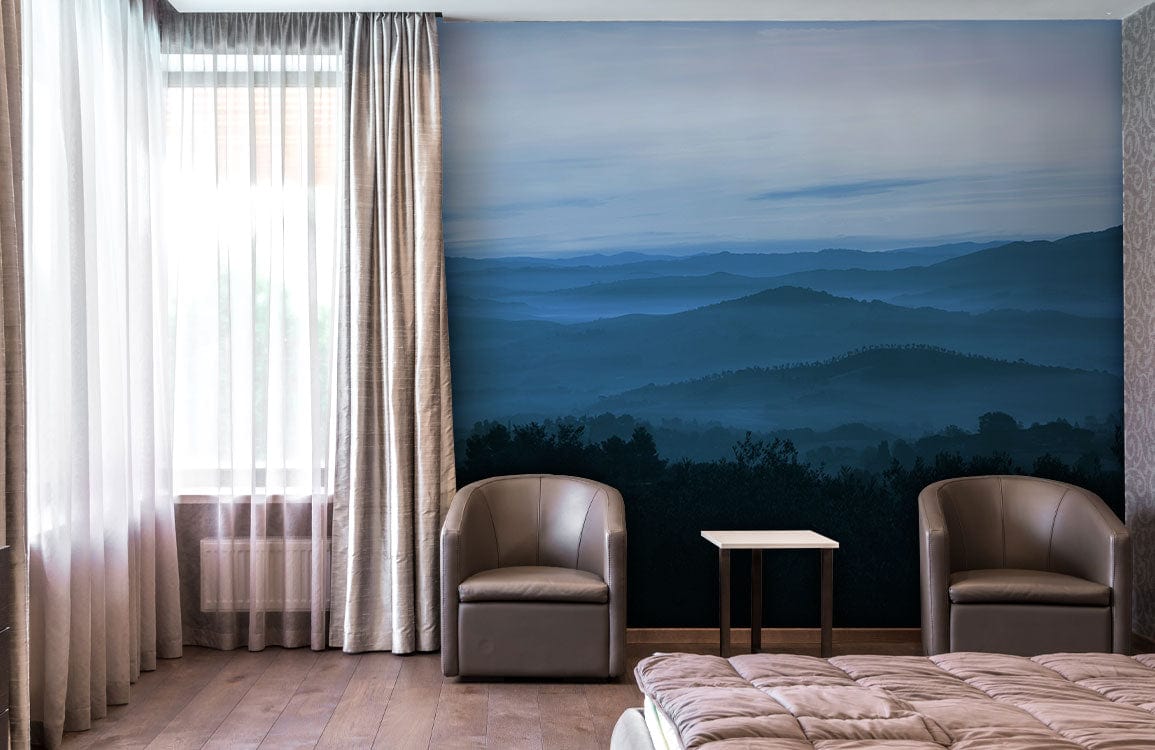Tranquil Blue Misty Mountains mural in stylish bedroom with taupe chairs, wooden flooring, and beige curtains.