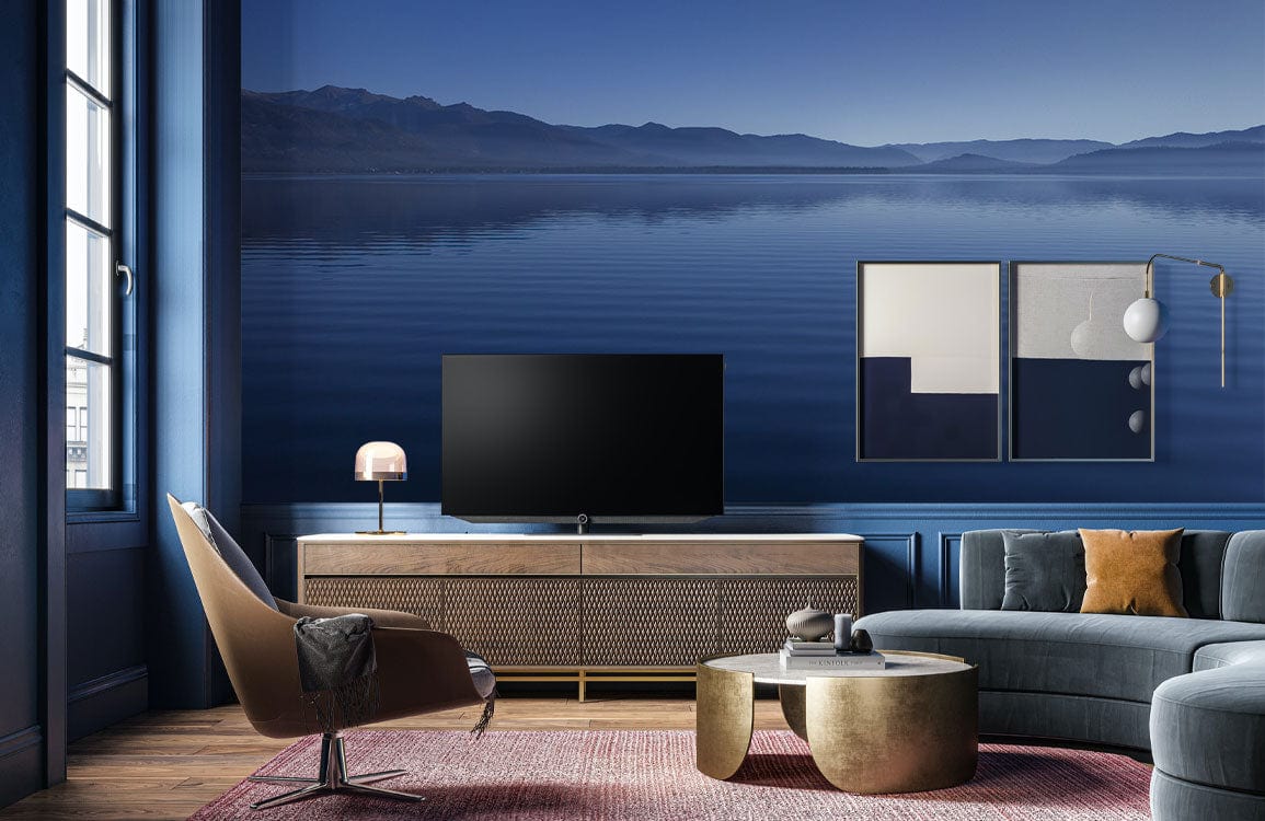 Serene Blue Lake Panorama Wallpaper in modern living room, blue sofa, wooden flooring, wall art, TV.