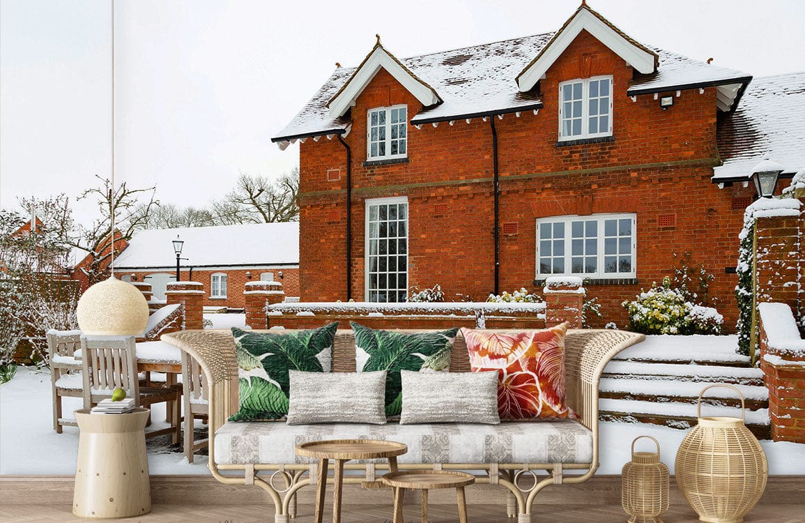 Snowy English countryside mural wallpaper with brick house, wicker sofa, green cushions, wooden flooring.