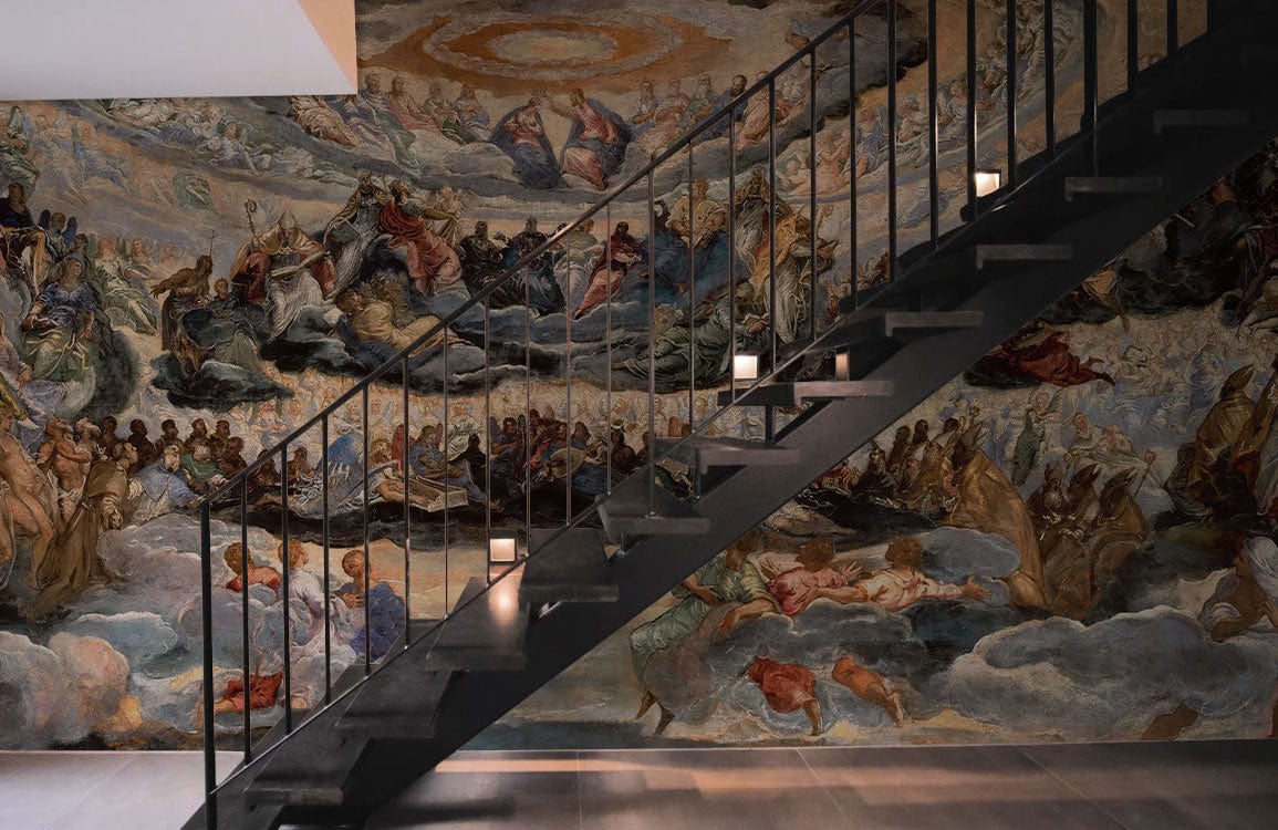 Ethereal Renaissance Heaven Mural Wallpaper beneath black staircase in modern room with wooden flooring.