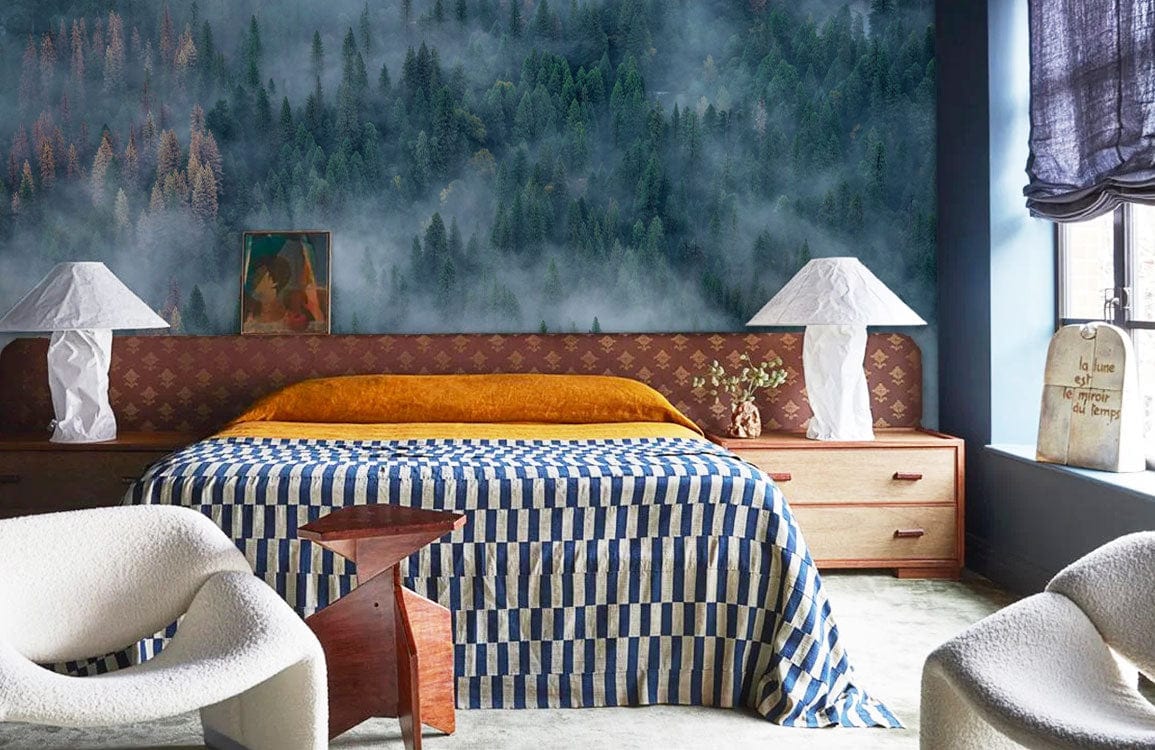 Foggy Forest mural wallpaper behind bed with striped bedding, white chairs, wooden side tables, white lamps.