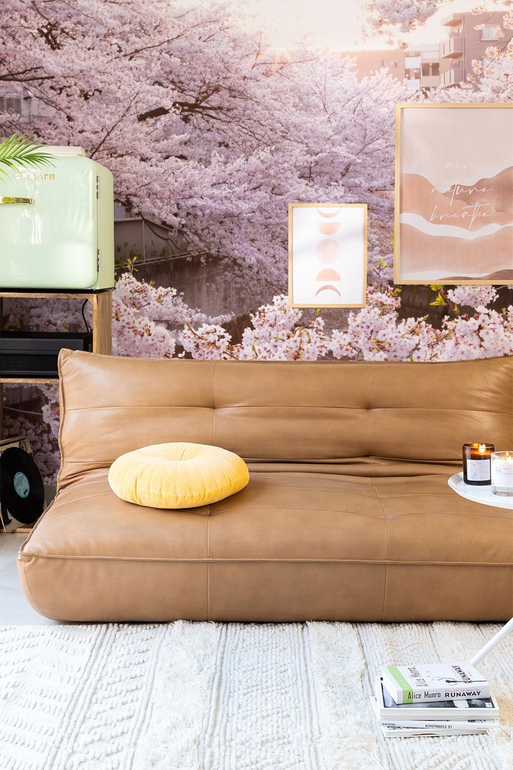 Elegant pink blossom mural wallpaper showcasing cherry blossoms, leather sofa, cream rug, wall art, and vase.