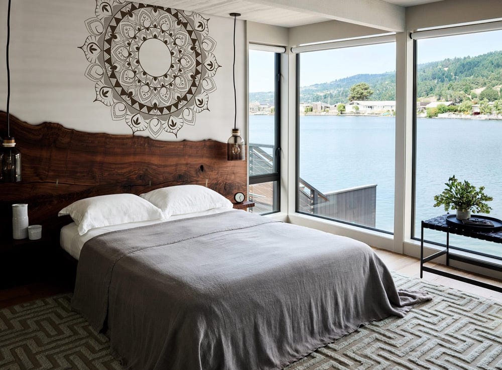 Intricate brown mandala pattern wallpaper in lakeview bedroom, grey bedding, wooden headboard, geometric carpet.