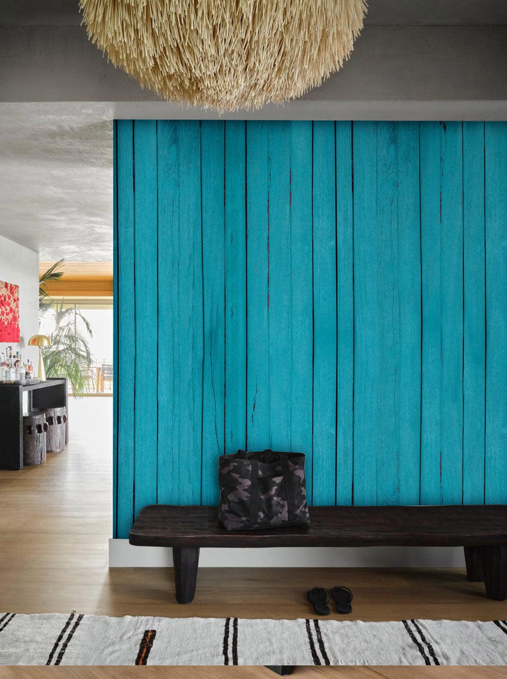 Rustic turquoise wallpaper in coastal decor, dark wooden bench, modern rug, hardwood floor, wicker pendant.
