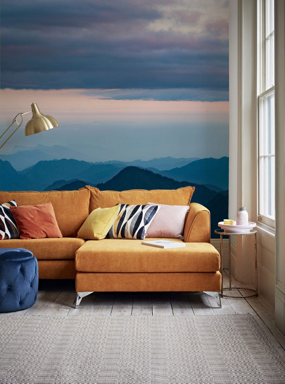Serene Mountain Vista Wallpaper in living room with orange sofa, blue pouffe, wood flooring.