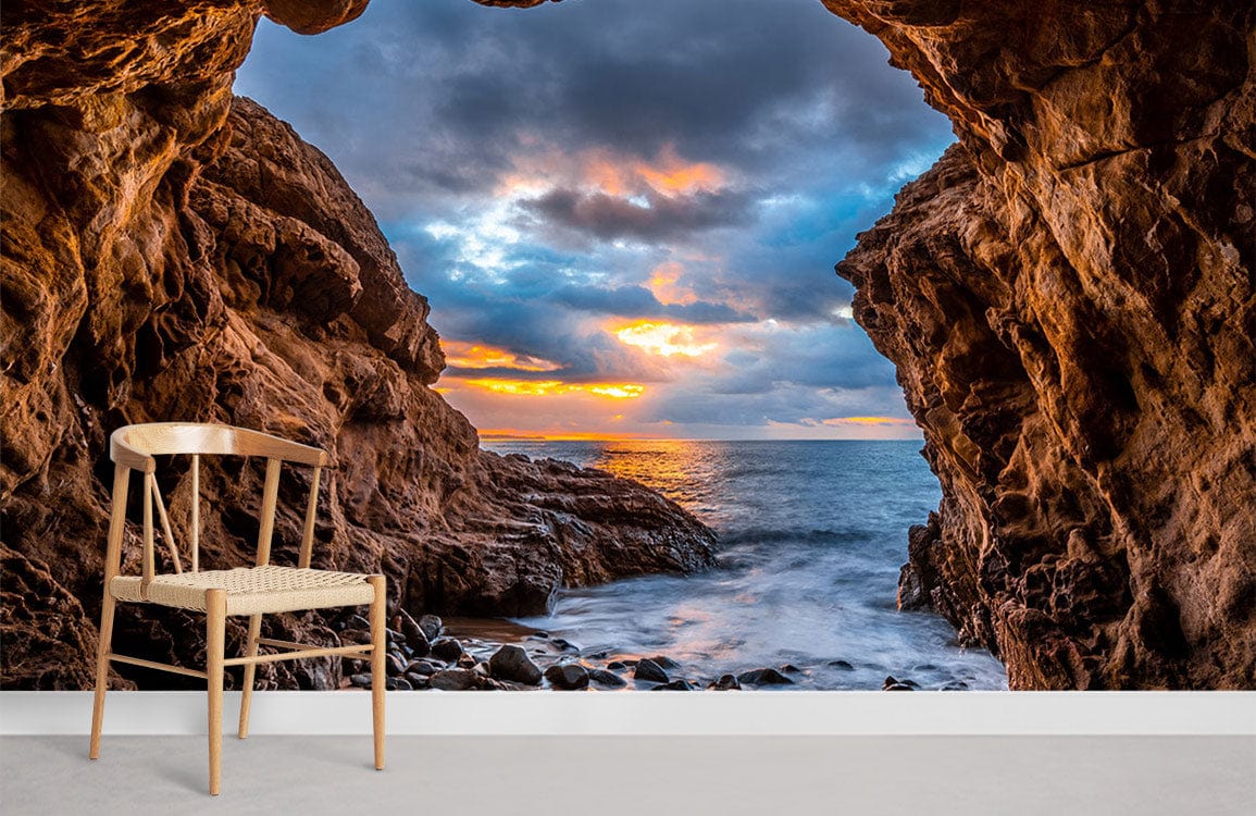 Stunning Ocean Cave Sunset Mural Wallpaper, vibrant coastal colours, wooden chair, minimalist style room.