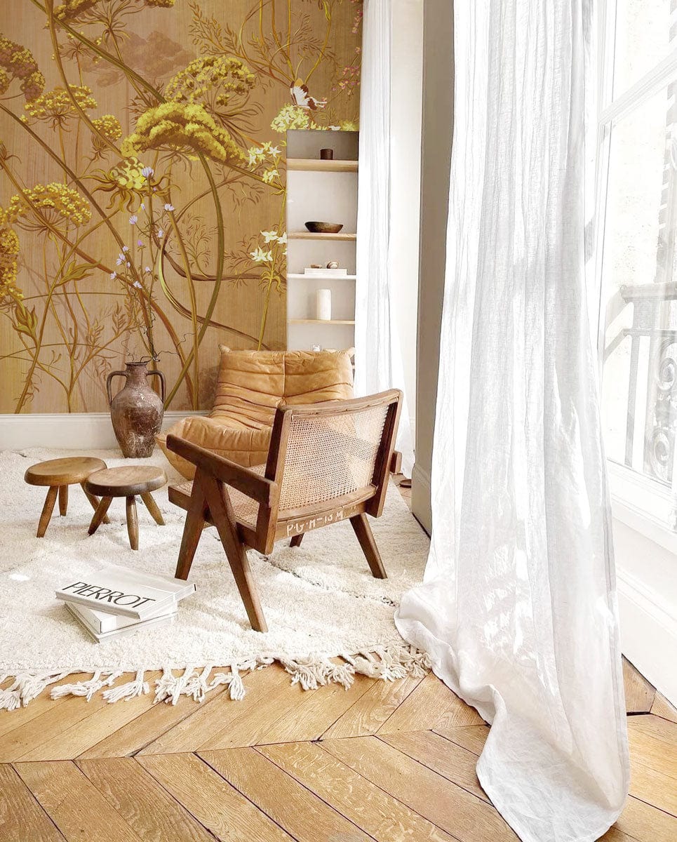 Golden Botanical Meadow Mural Wallpaper in vintage floral design; neutral chair, wooden flooring, airy curtains.