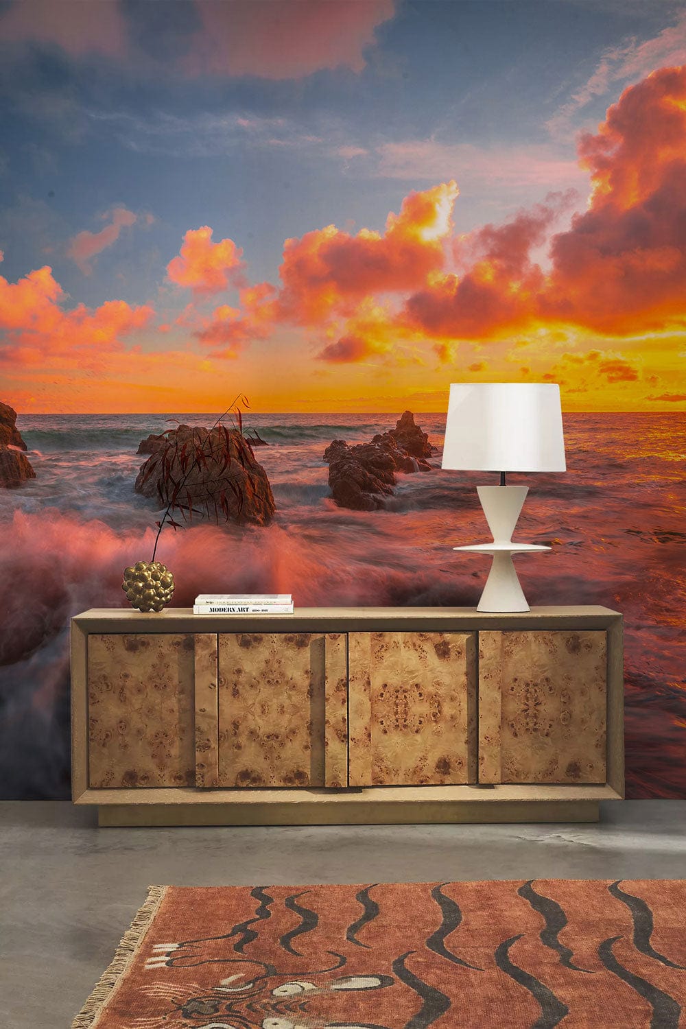 Vibrant Sunset Seascape Mural Wallpaper with wooden cabinet, white lamp, patterned rug, concrete floor.
