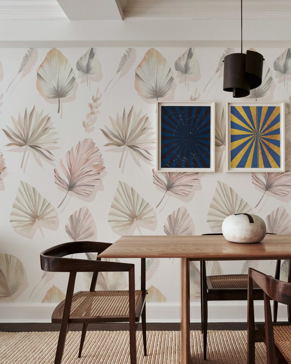 Elegant pastel botanical leaf wallpaper in dining room, wooden table, dark chairs, hanging light fixture.