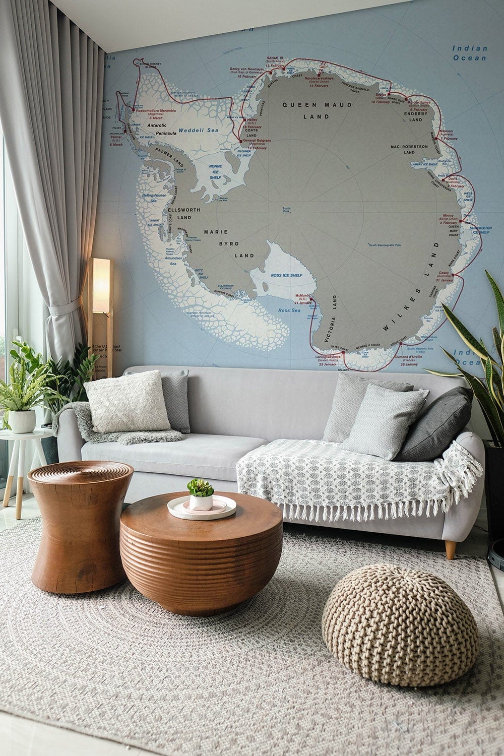 Vintage Antarctic Map Mural in modern lounge with grey sofa, round wooden tables, and knit pouffe.