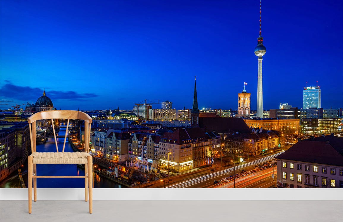 Berlin Night Skyline mural wallpaper with wooden chair; vibrant cityscape, deep blues, light grey floor.