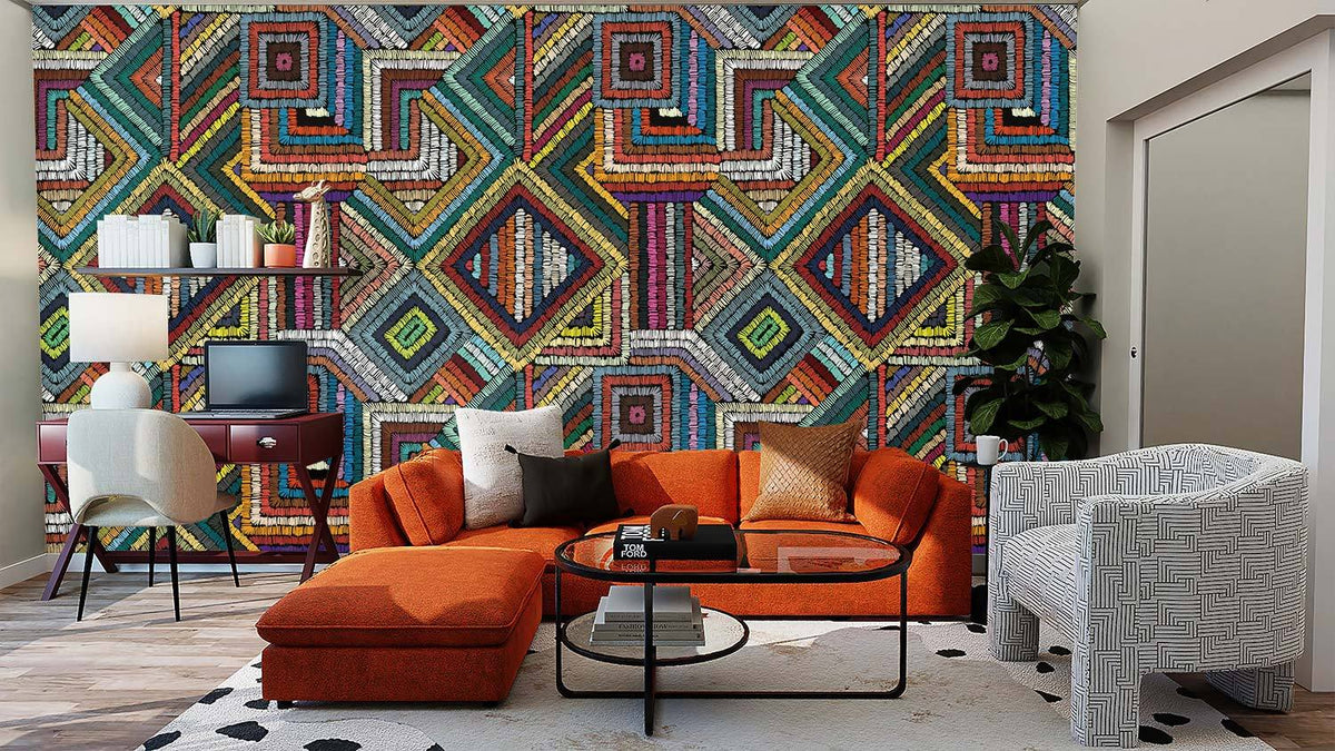 Vibrant geometric tribal pattern wallpaper, multicolour decor, orange sofa, white armchair, wood flooring.