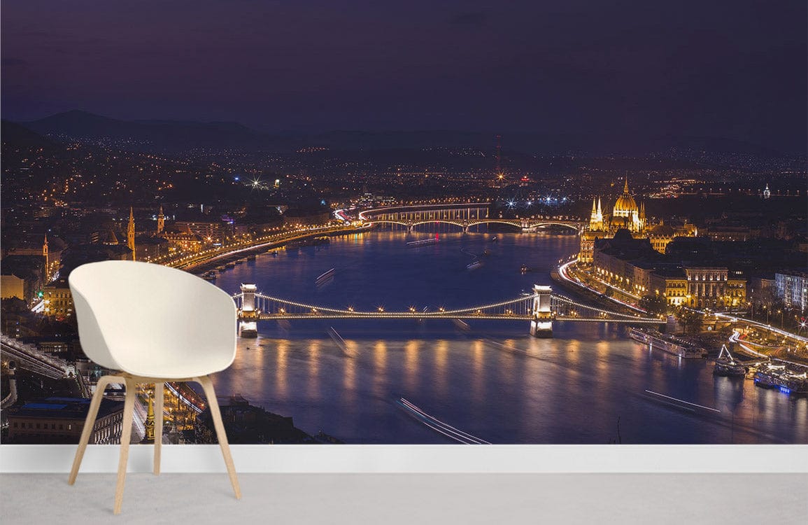Illuminated river cityscape mural wallpaper with bridges, white modern chair, grey flooring, living room.