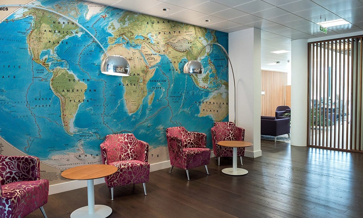 Vintage World Map Mural Wallpaper, blue cream tones, office setting, pink patterned chairs, wood flooring.