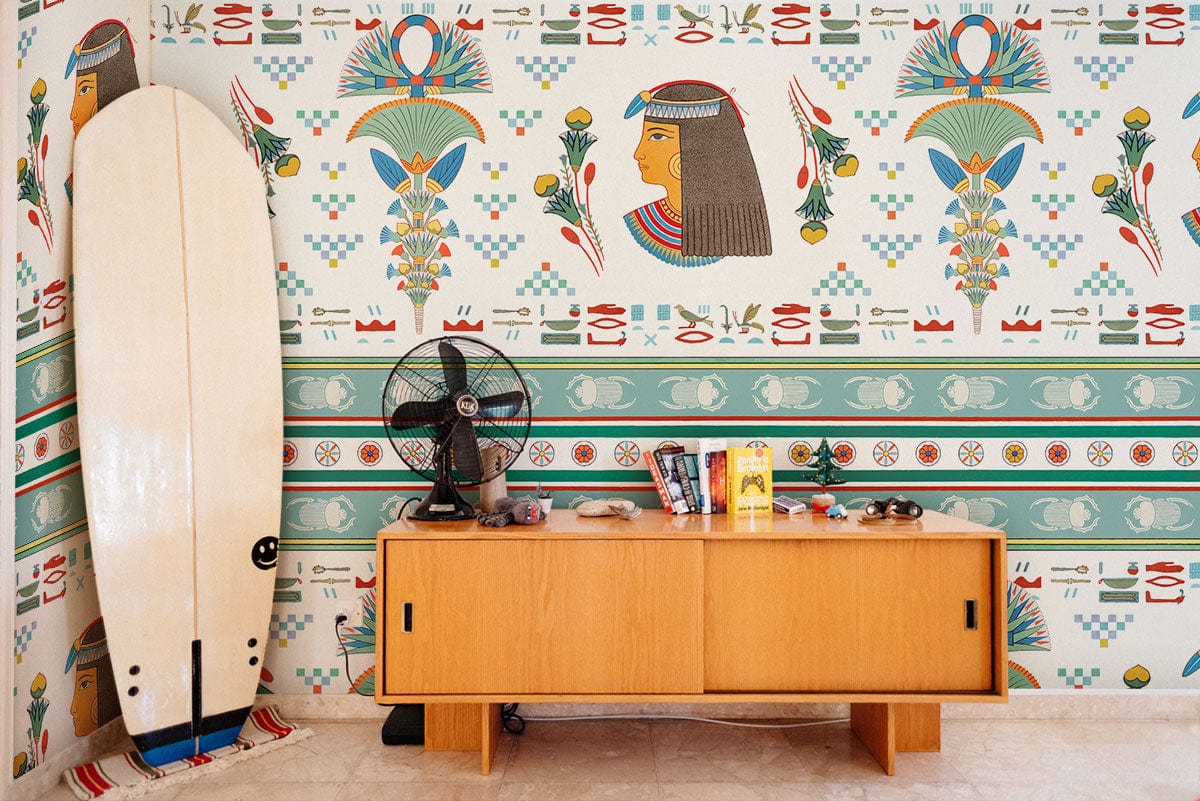 Egyptian Revival vintage wallpaper in room with wooden sideboard, surfboard, fan, and tiled flooring.