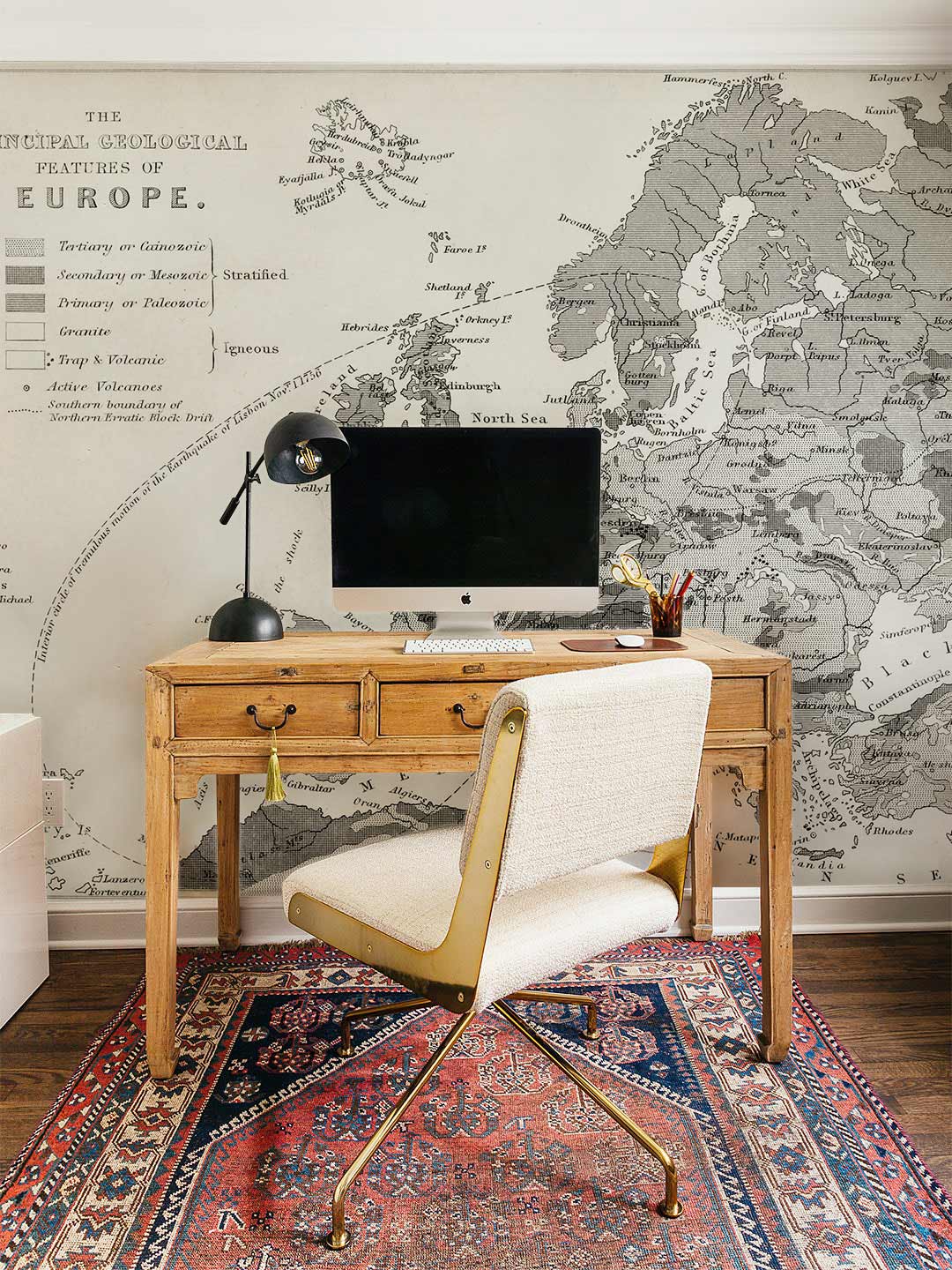 Vintage European geological map mural wallpaper, wooden desk, beige chair, patterned rug, home office.