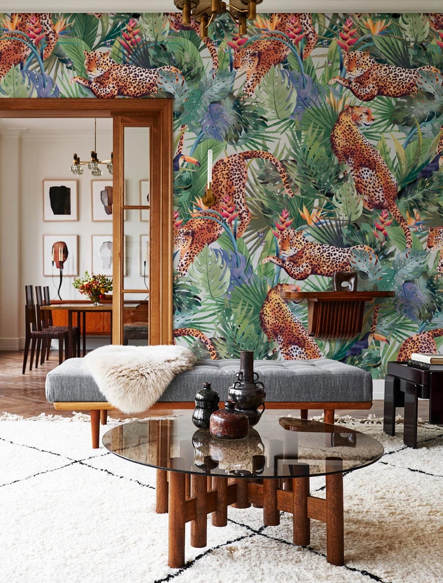 Tropical jungle leopards wallpaper in living room with grey bench, glass table, and vintage chandelier.