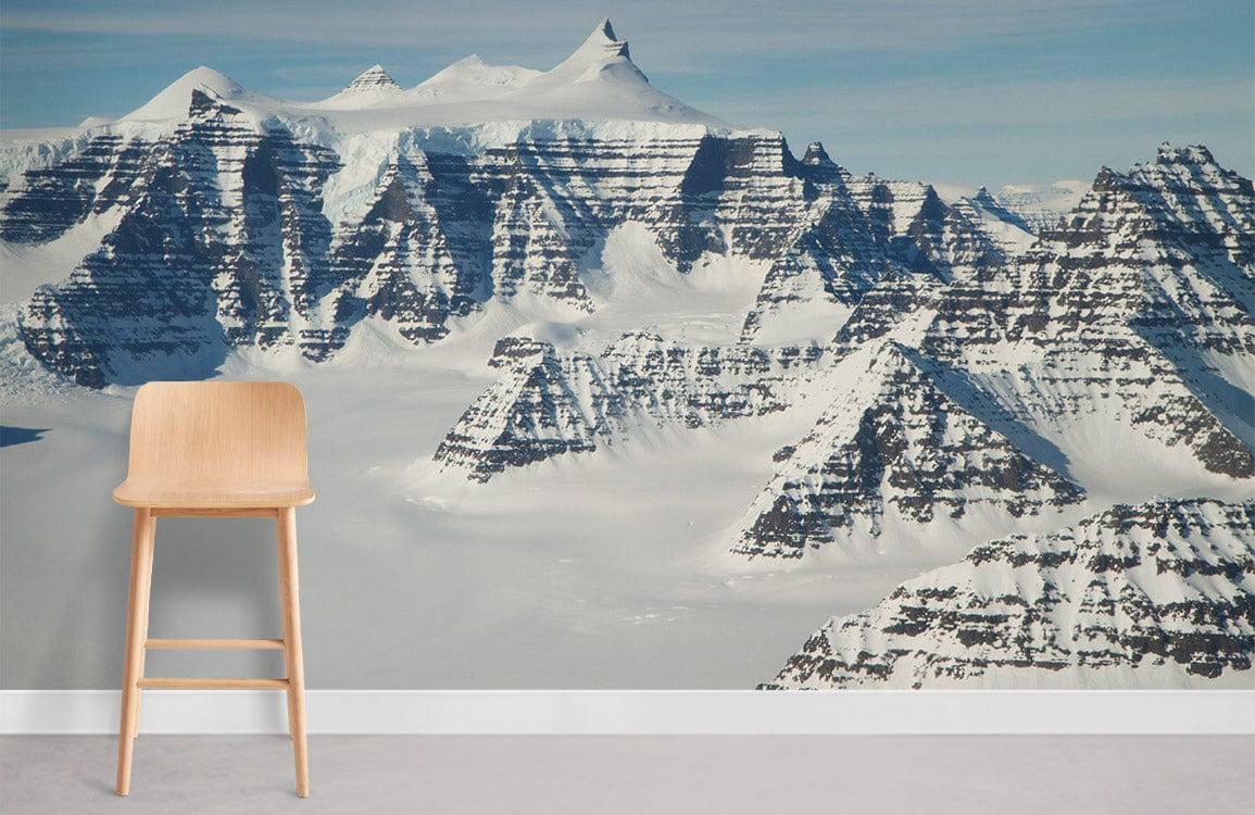 Majestic snow-capped mountain mural wallpaper, crisp white and blue; light wooden chair, concrete flooring.