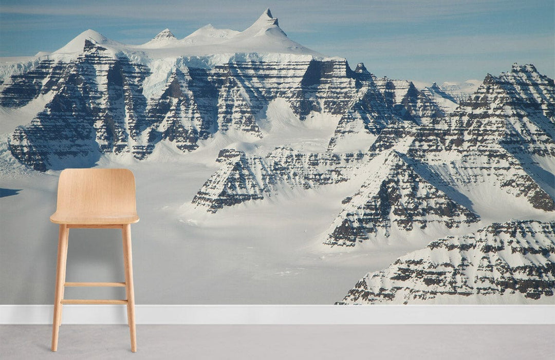 Majestic snow-capped mountain mural wallpaper, crisp white and blue; light wooden chair, concrete flooring.