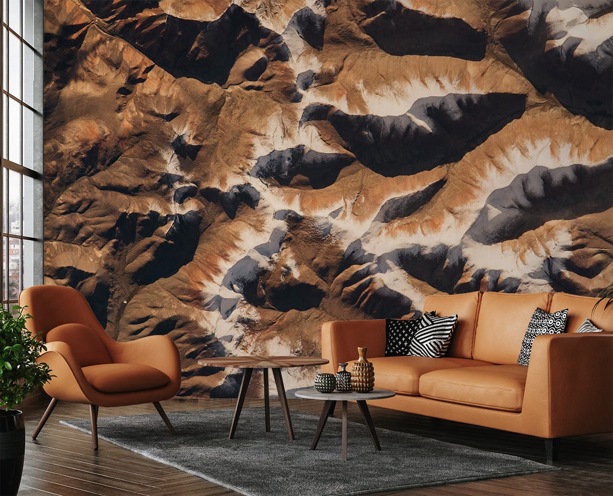 Abstract Earth Tones Geometric Mountainscape Mural Wallpaper with brown sofa, modern armchair, grey rug, wooden floor.