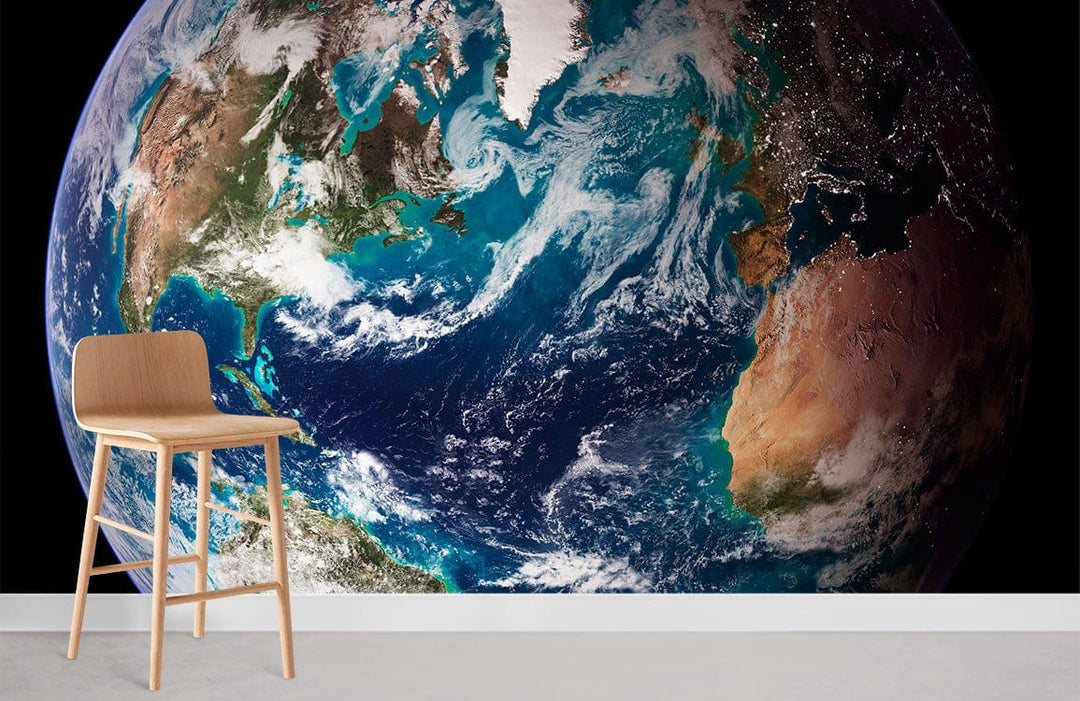 Stunning Earth mural wallpaper with vibrant blue-green planet and light wood chair, white skirting board.