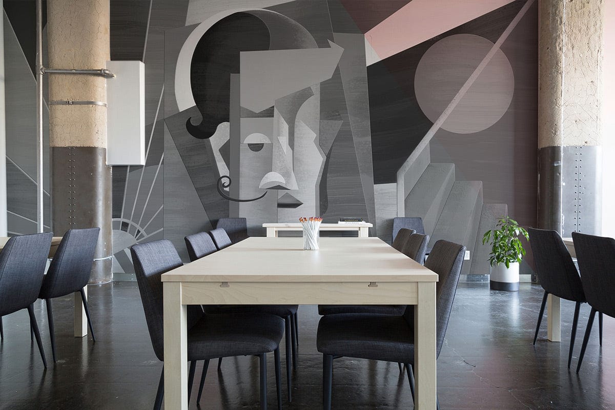 Monochrome geometric Art Deco mural in dining room, black chairs, light wooden table, concrete flooring.