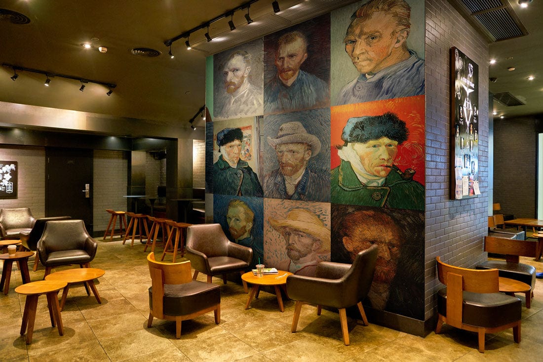 Vincent Van Gogh inspiring mural wallpaper with leather chairs, wooden tables, and tiled flooring in cafe.