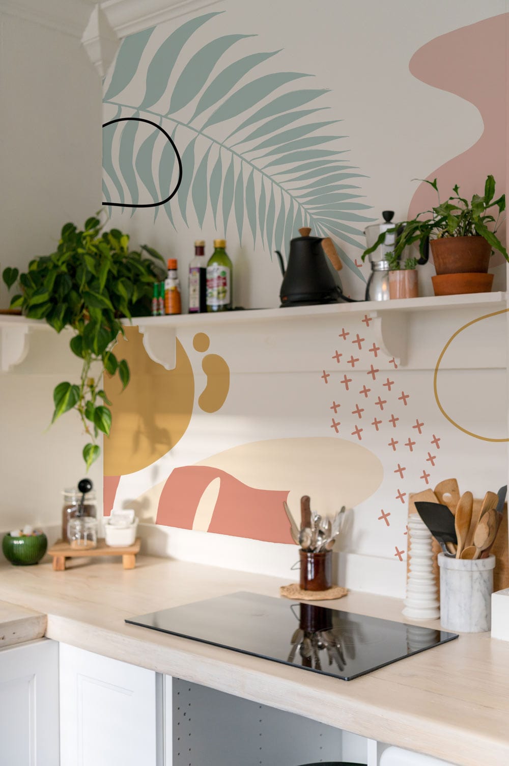 Tropical abstract botanical pastel wallpaper mural in soft peach and sage tones, kitchen setting, light woodworktop.