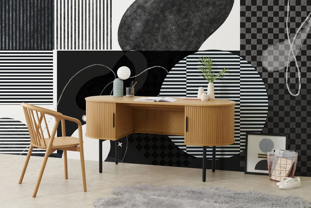 Monochrome abstract geometric wallpaper with wooden desk, chair; modern interior design, grey rug, light flooring.