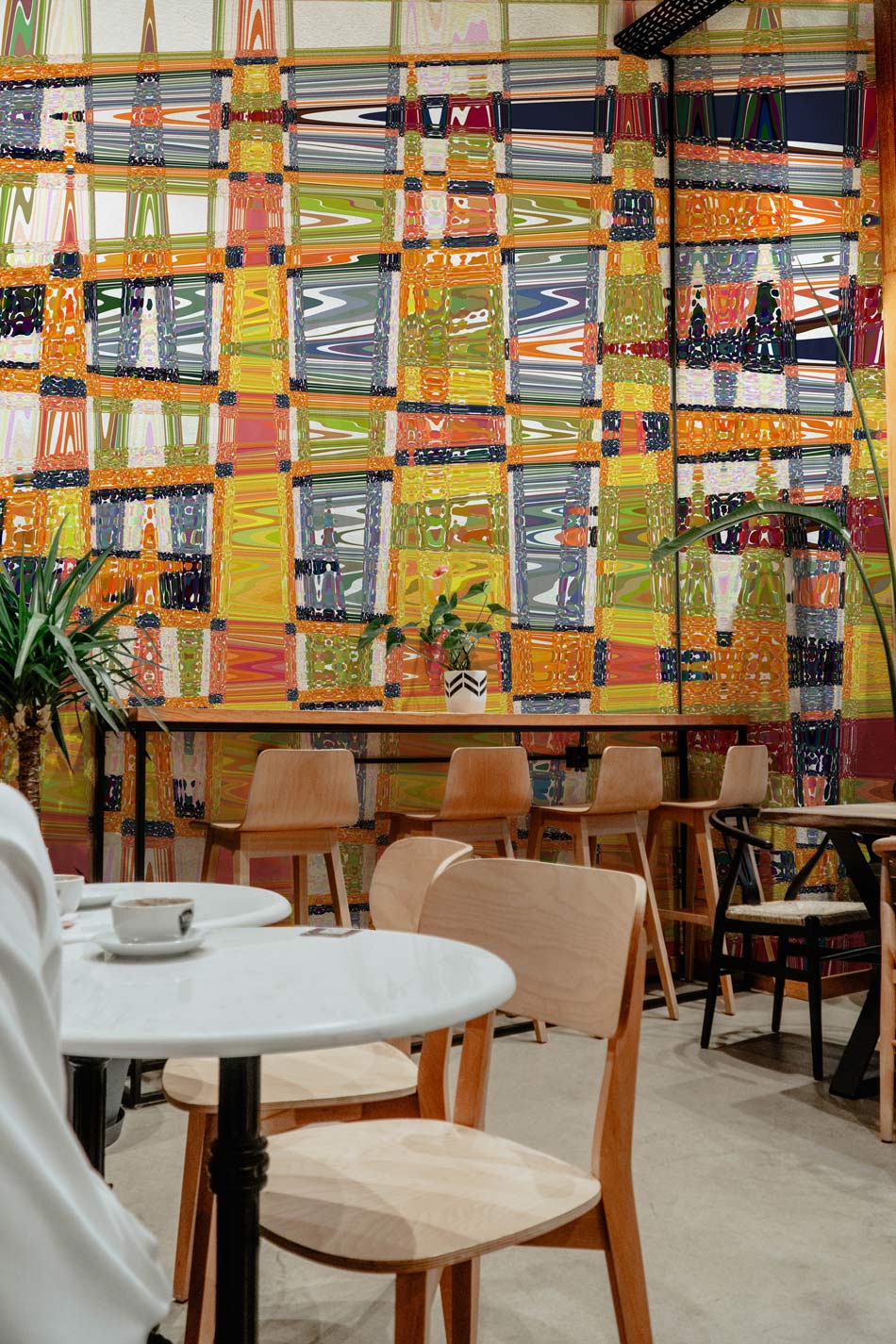Vibrant geometric mural wallpaper in modern café setting with wooden chairs and tables, accenting design features.