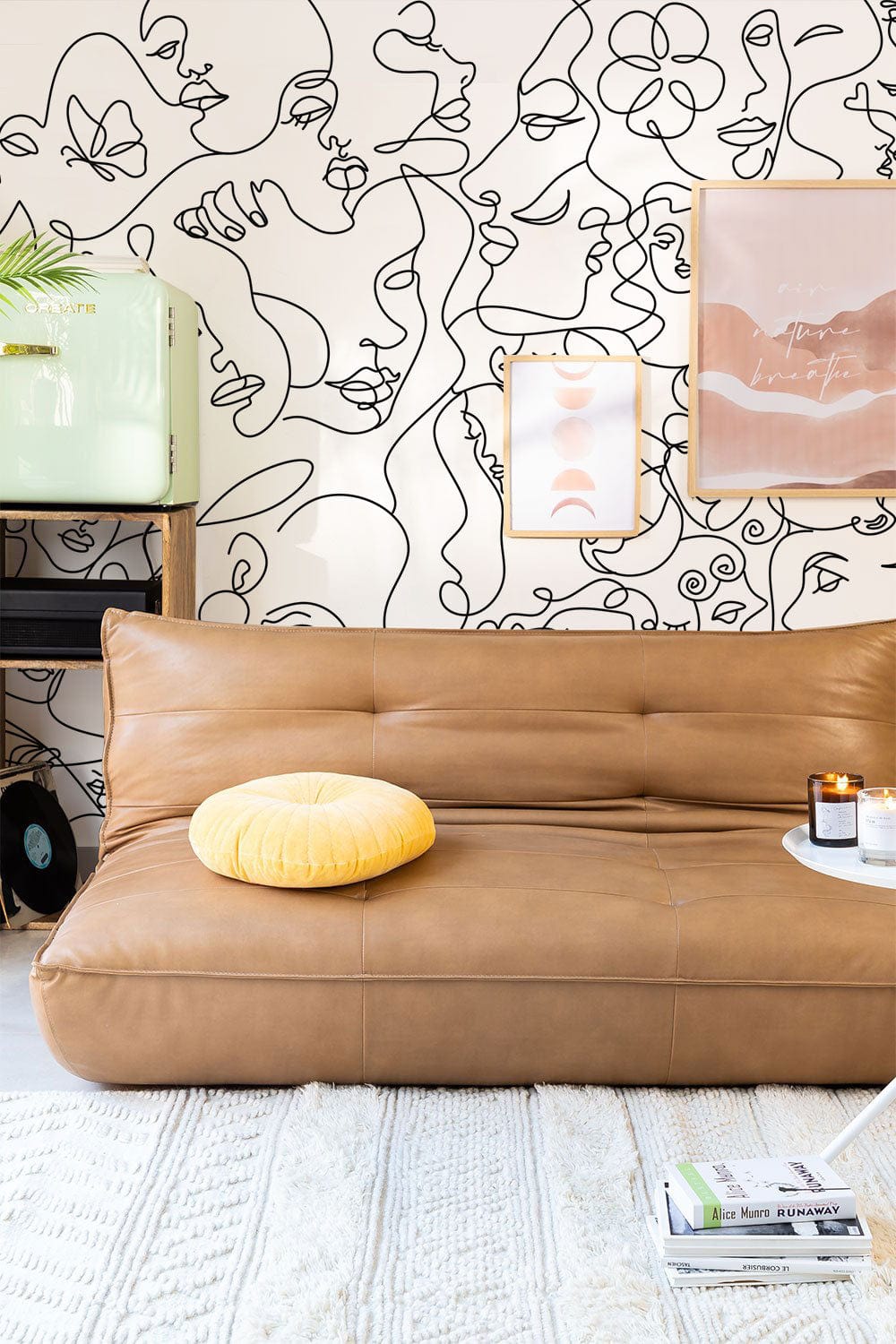 Monochrome abstract faces mural in contemporary living room with tan sofa, light rug, and wall art.