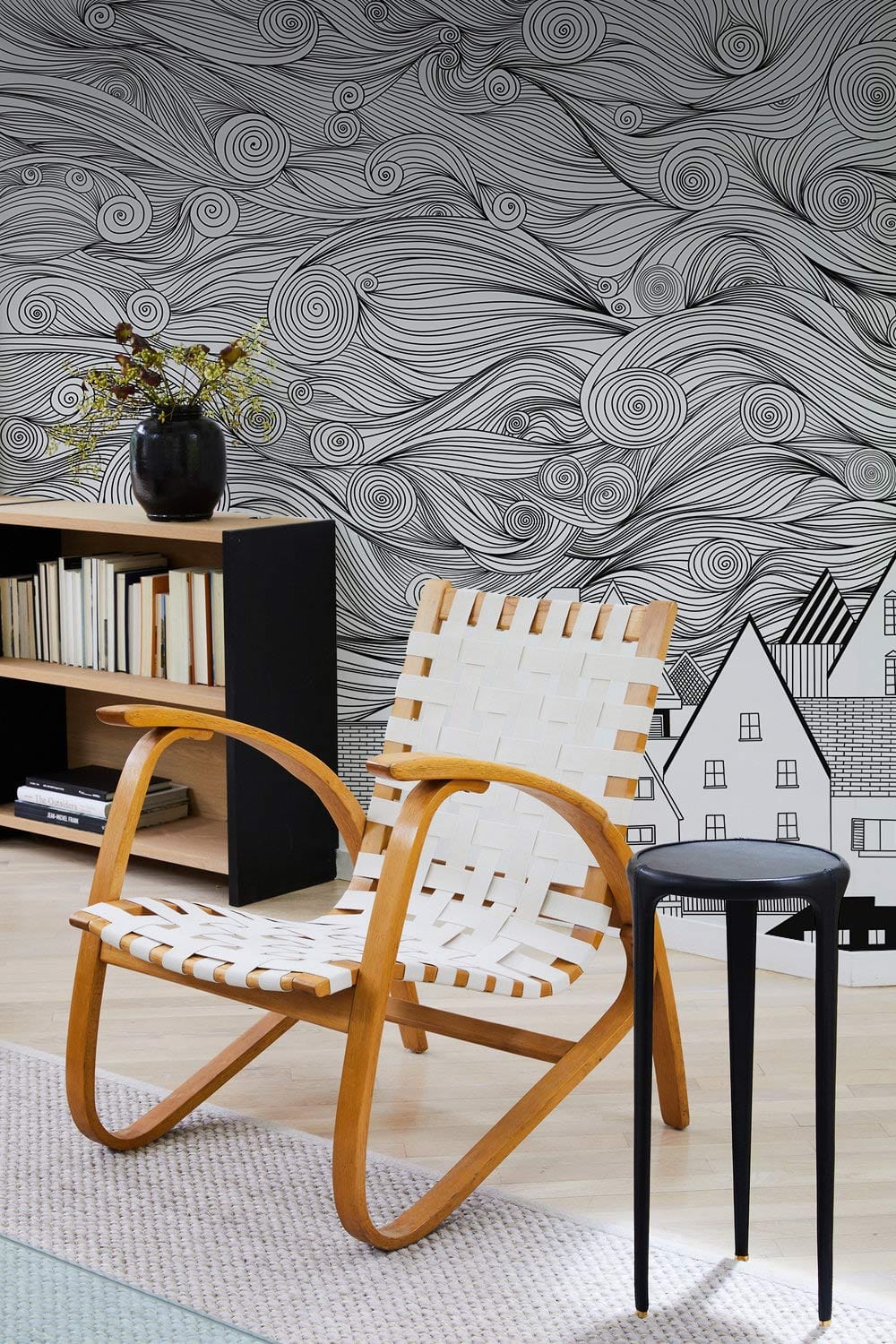Black & White Whimsical Town Mural Wallpaper with abstract sky, wooden chair, black side table.