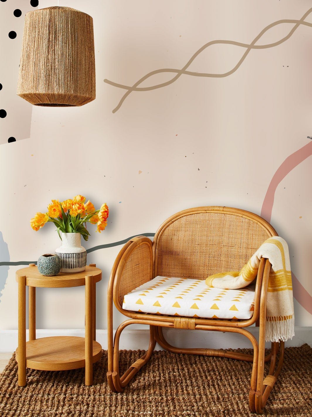 Abstract geometric pastel wallpaper with rattan chair, wicker lampshade, and round wooden side table.