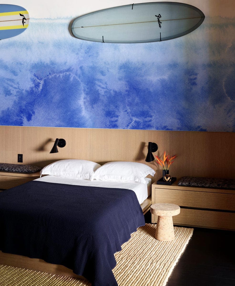 Oceanic Blue Watercolour Mural Wallpaper in bedroom with surfboards, wooden furniture, and woven rug.
