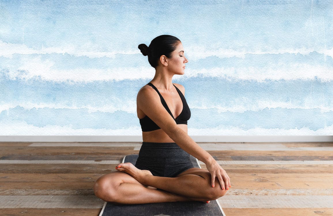 Woman doing yoga in modern living room with Tranquil Blue Watercolour Ombre Wall Mural, wooden flooring.