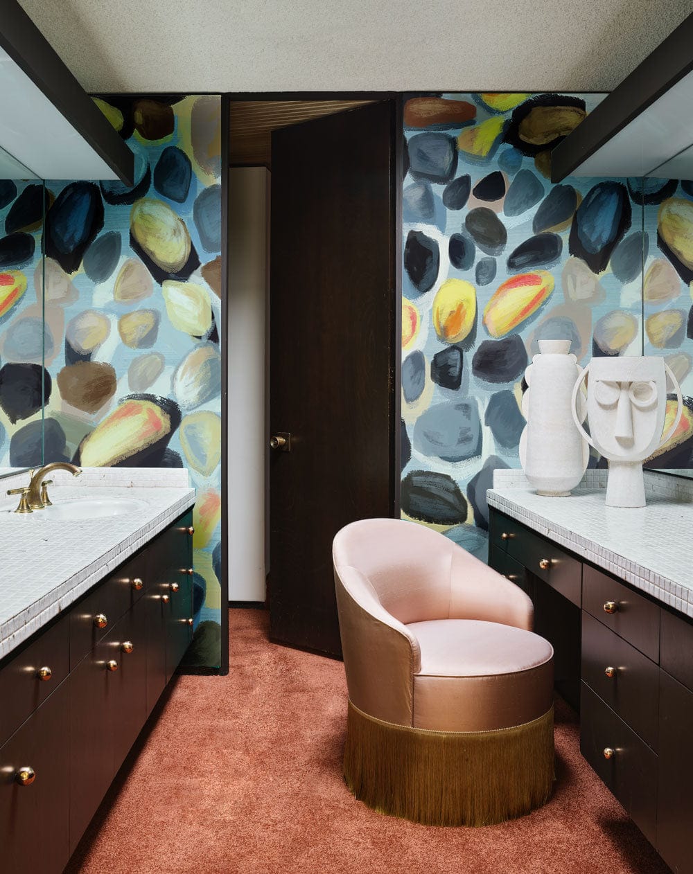 Multicoloured watercolour pebble pattern wallpaper in bathroom with pink chair, dark cabinets, and carpet flooring.