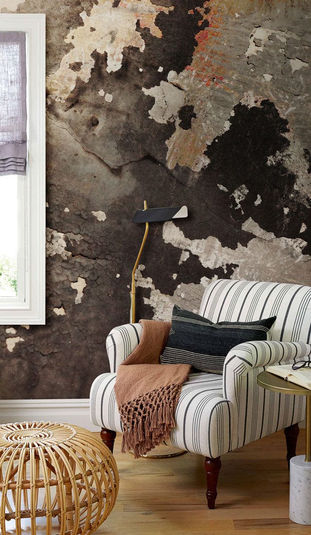 Armchair with striped upholstery, wicker ottoman, wooden flooring, earthy textured wallpaper enhances lounge ambience.