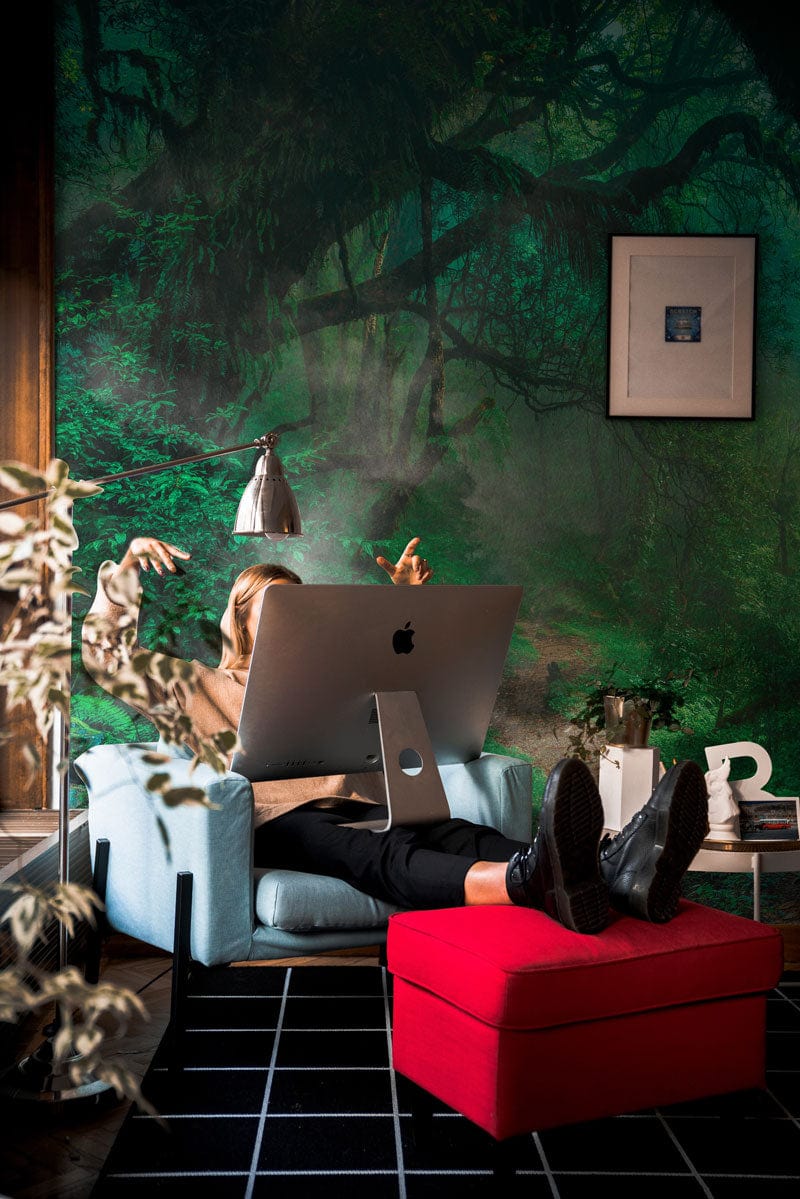 Enchanted Forest Green mural wallpaper in a modern room with blue chair, red footrest, and artwork.
