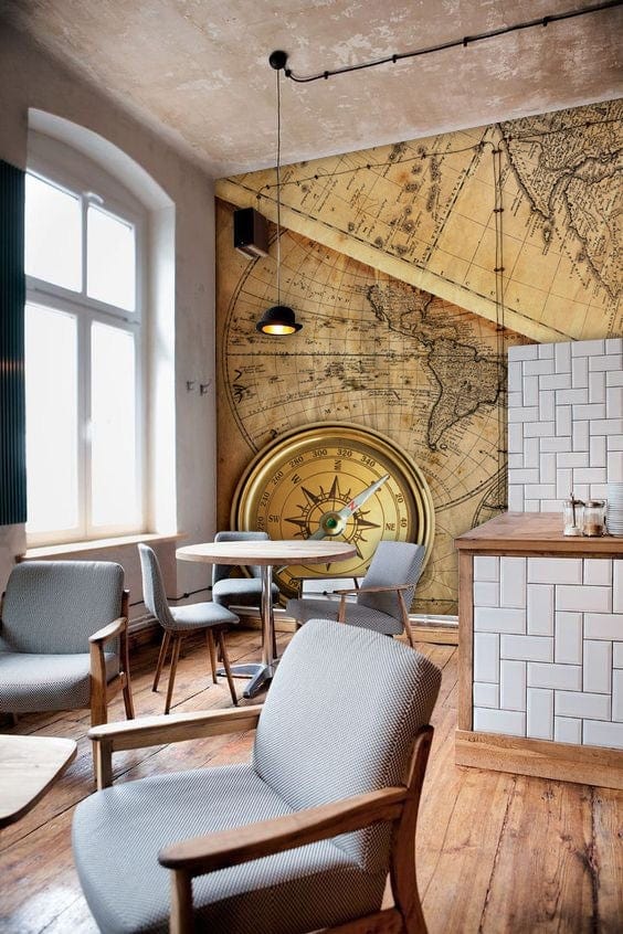 Vintage world map wallpaper with earthy tones in a stylish cafe, wooden flooring, grey chairs.